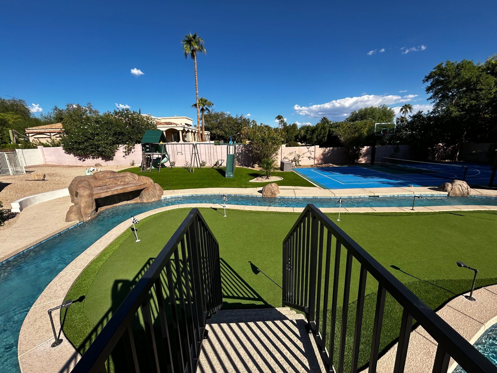 View down the bridge stairs toward the putting-green island, lazy river, sport court, and playground