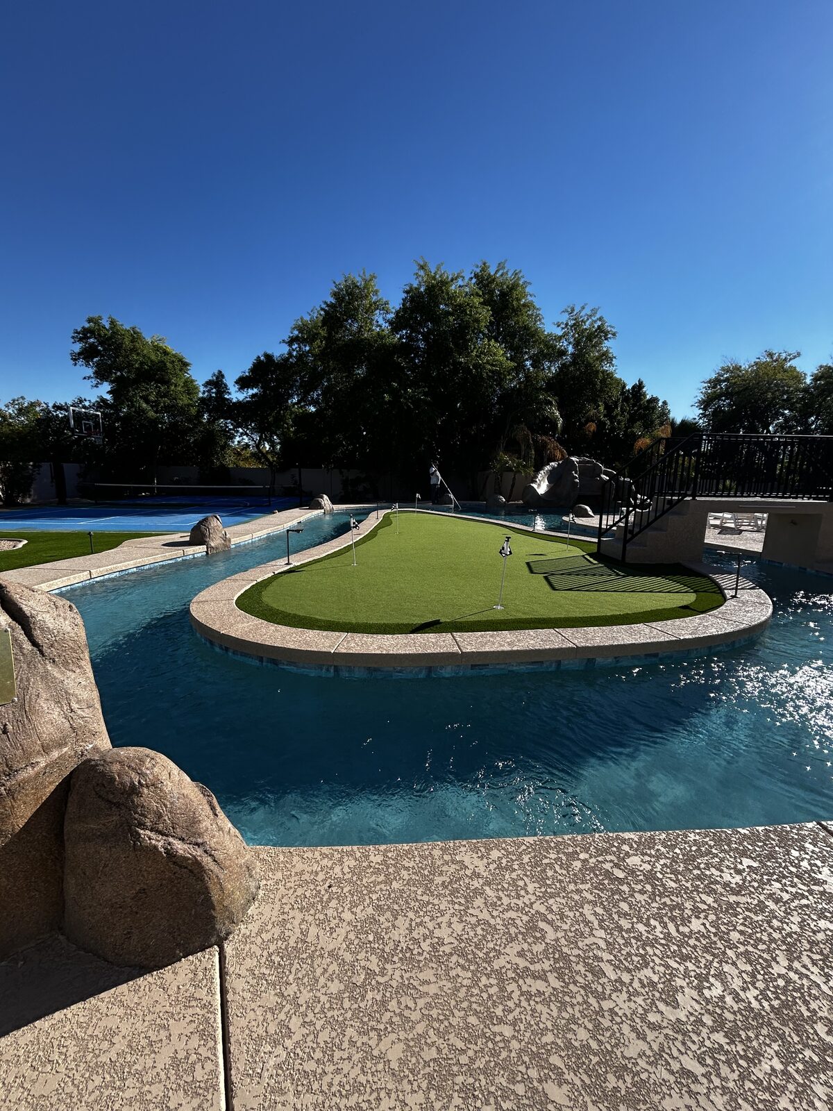 Ground-level view of the putting-green island ringed by the lazy river, with the bridge and rockslide grotto beyond