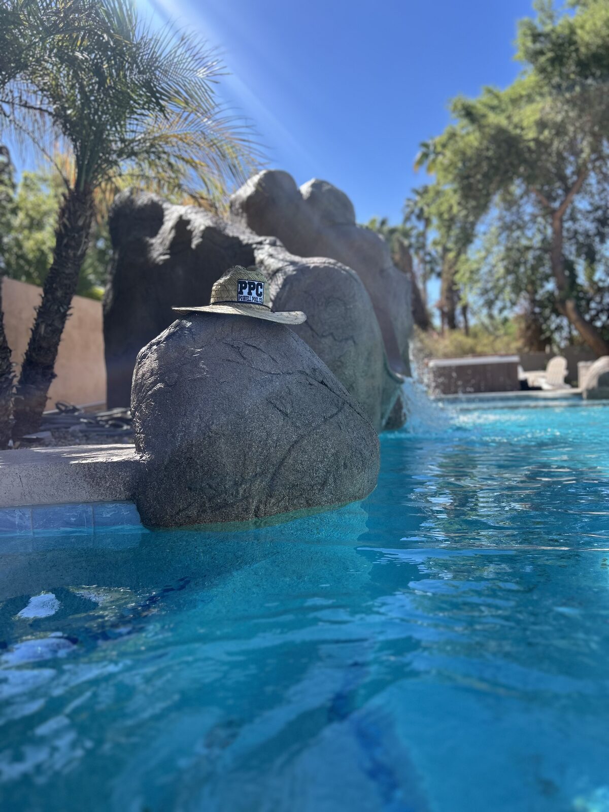 A straw hat with a Powell Pool Co patch resting on the rockwork beside the lazy river