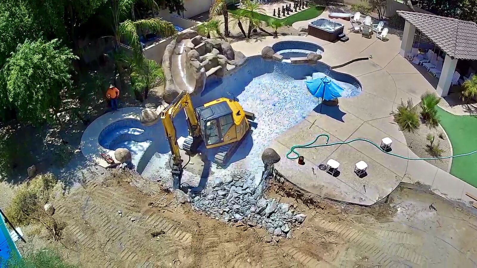 Aerial view of an excavator breaking out the old round pool, spa, and deck to begin the lazy river build