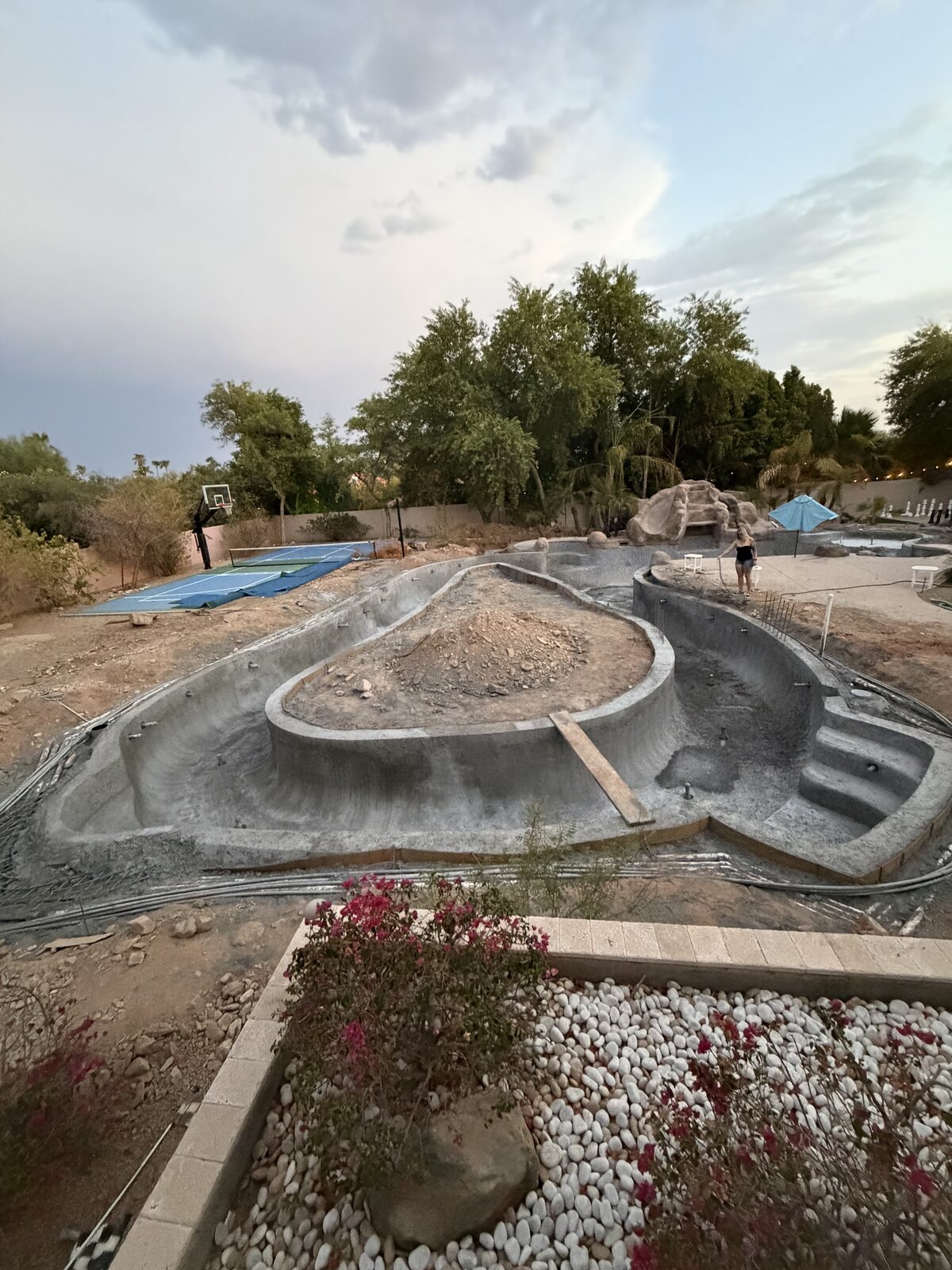 Wide view of the freshly shotcreted lazy river loop, with the future putting-green island still bare dirt in the middle