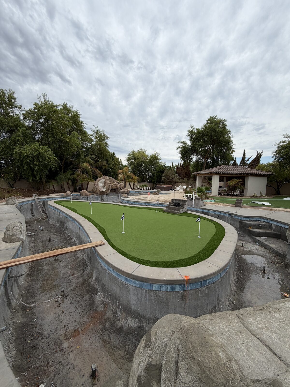 The putting-green turf installed and flagged, with blue tile coping going in around the still-empty river channel