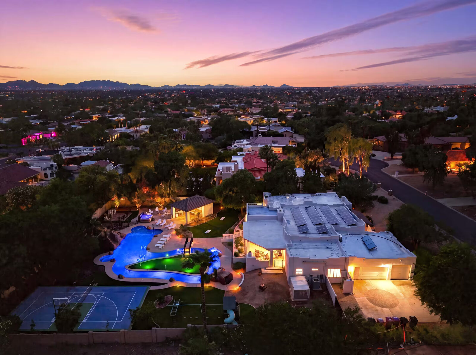 Wide aerial photo at blue hour, pulled back to show the backyard within the surrounding neighborhood and mountain skyline