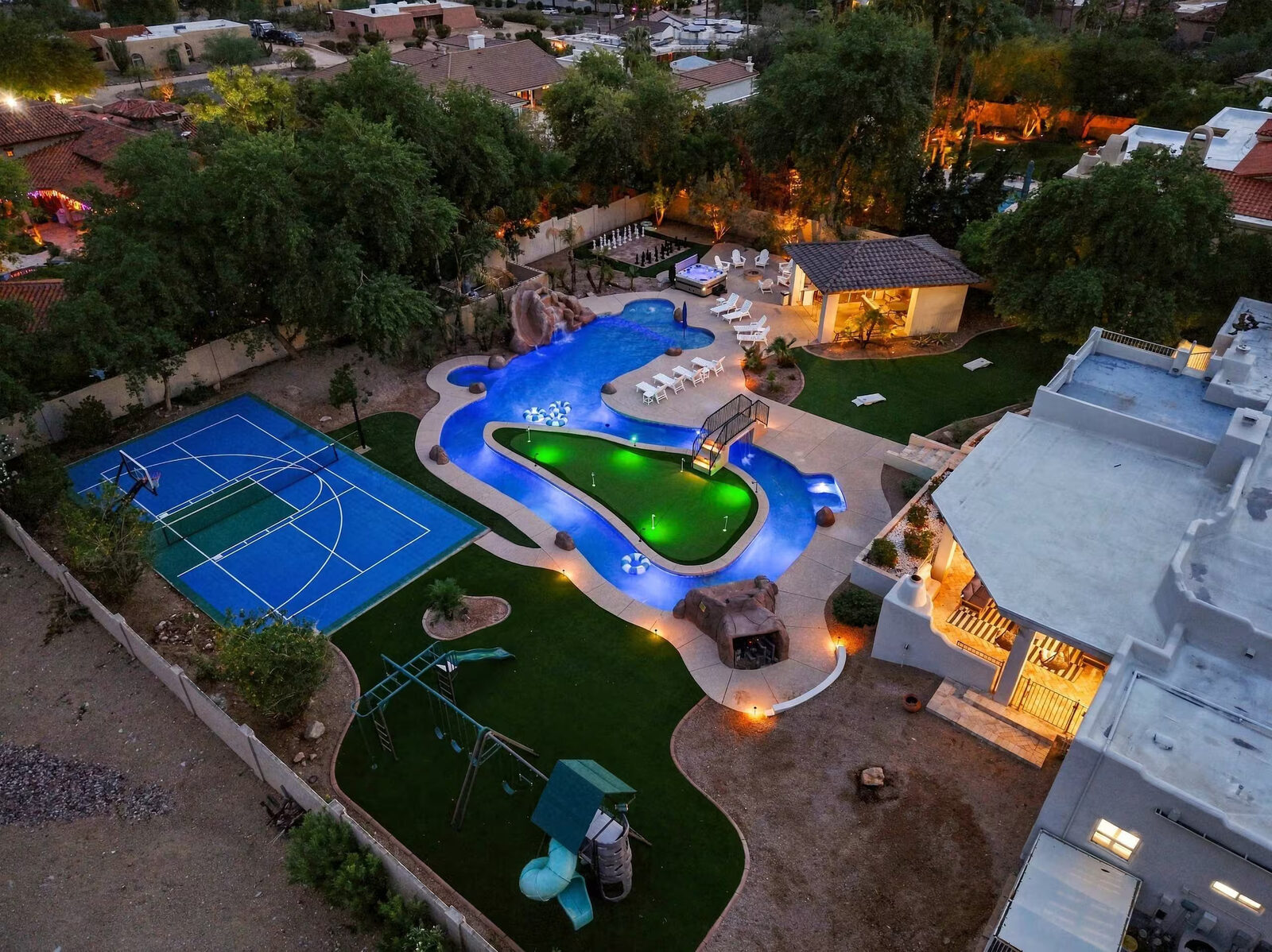 Angled aerial photo at dusk showing the pool, putting green, sport court, and playground together