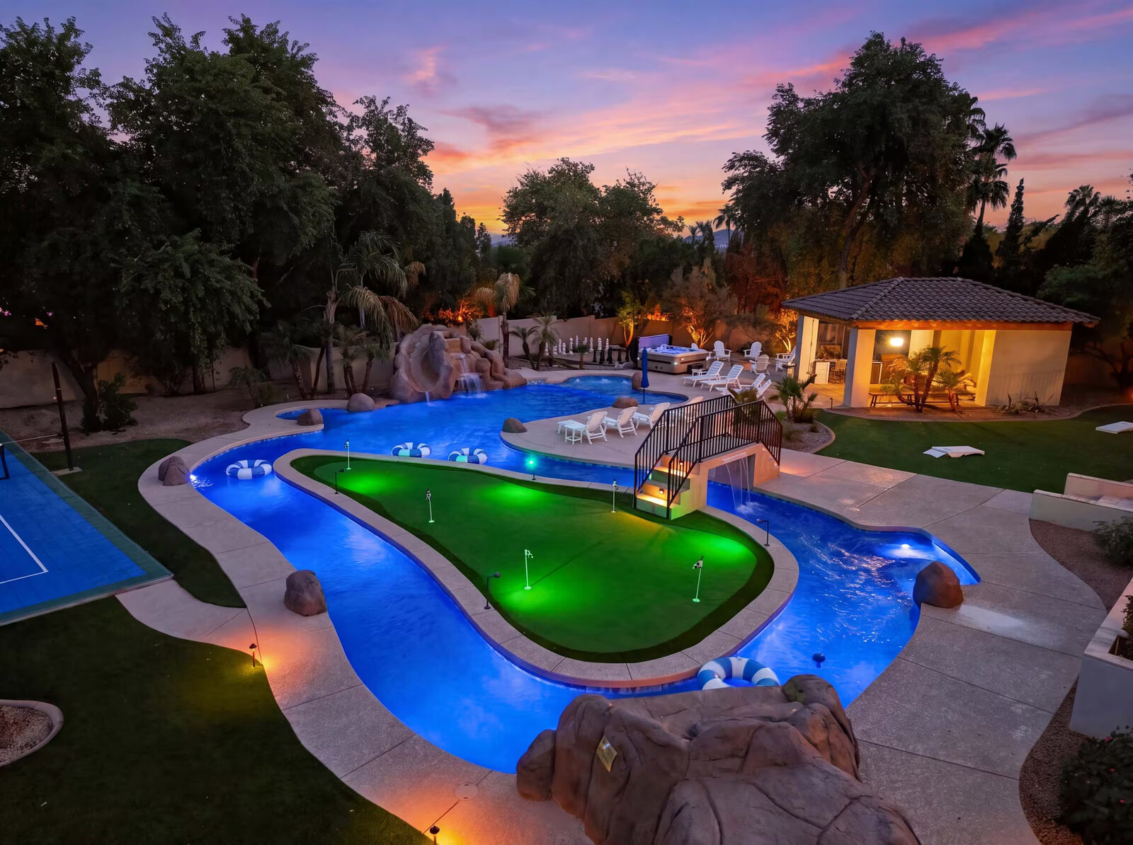 Wide ground-level photo of the backyard from the lawn at sunset, with the guest house, pool, and green in frame