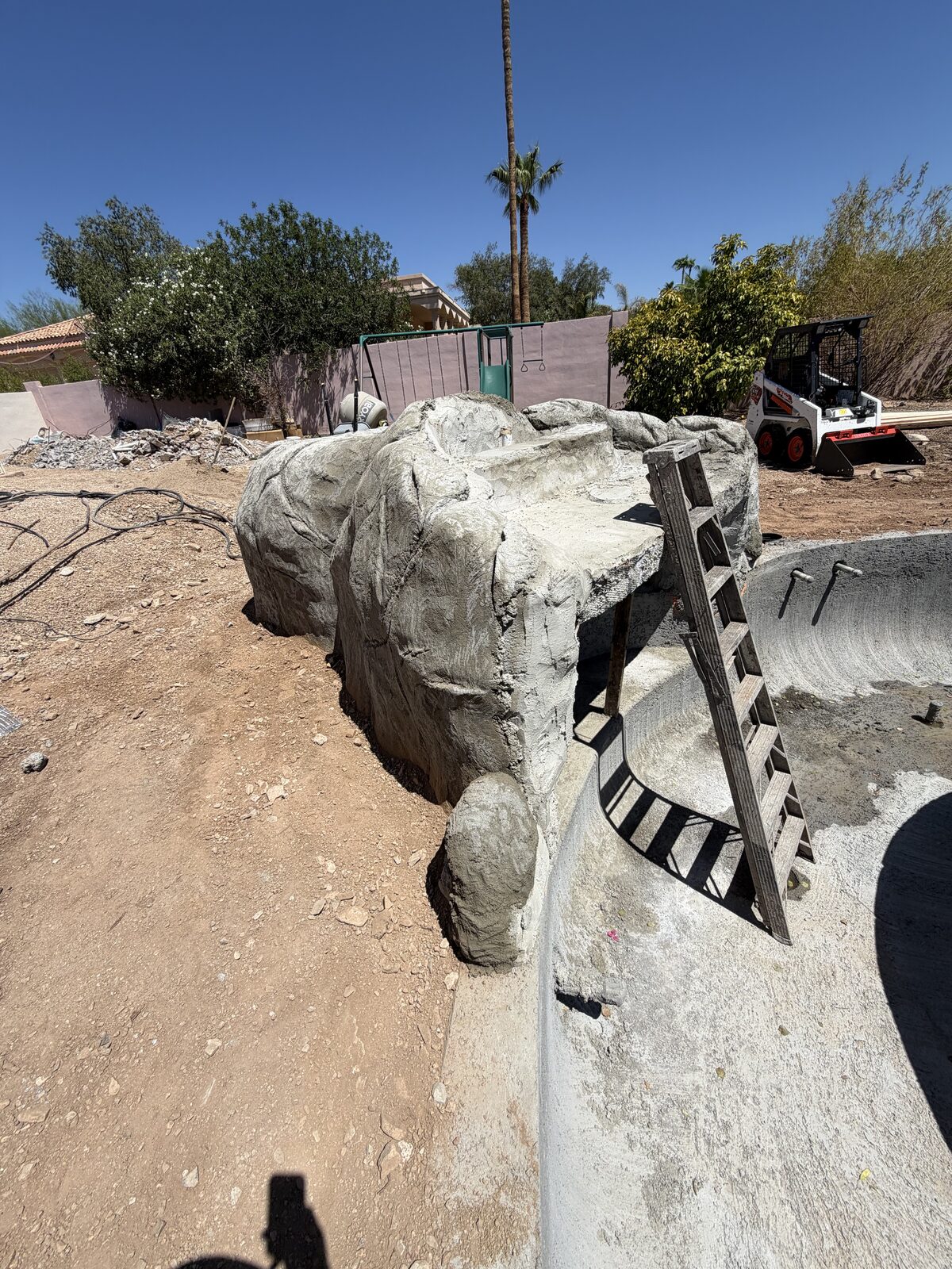Close view of the new waterfall feature's rockwork form taking shape, with a skid-steer in the background