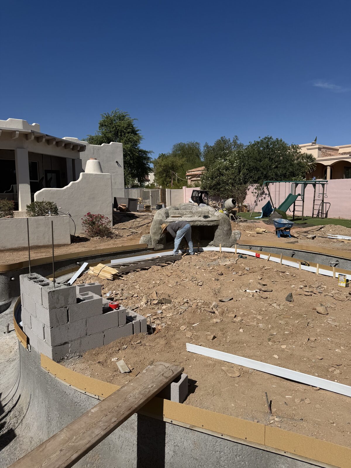 Cinder block wall forming the shape of the new lazy river channel, with the house visible beyond